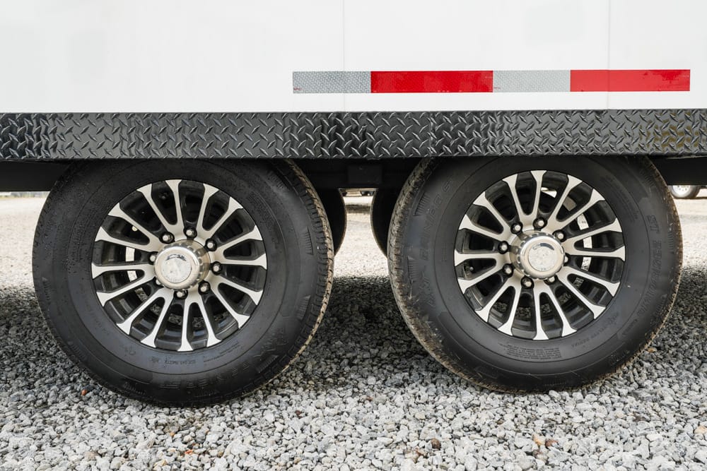 Dual wheels on a cargo trailer, with diamond-plate side and red/white reflective strip above the wheels.