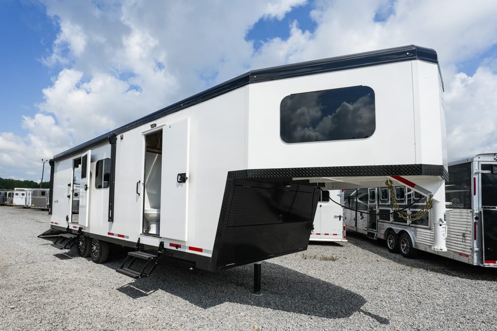White fifth-wheel RV trailer on a gravel lot with exterior stairs lowered and doors open, set among other trailers.