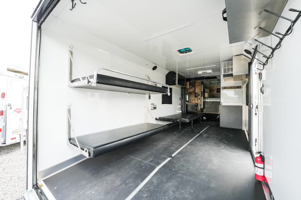 Interior of an empty ambulance showing two foldable medical cots along the left wall and equipment at the far end, ready for patient transport.