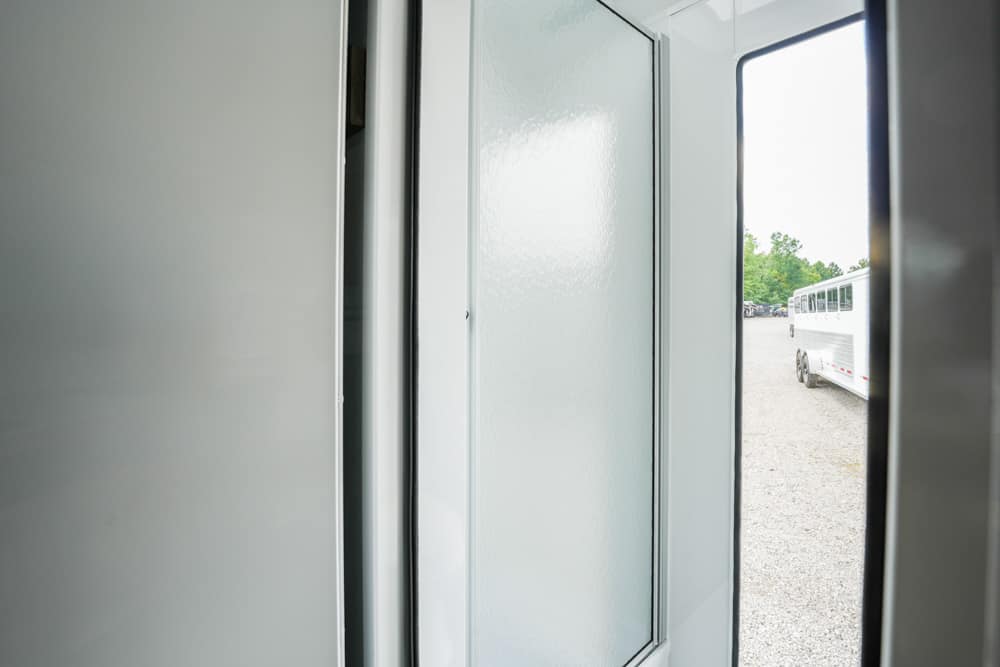 Interior doorway in a light-colored trailer, looking out at a gravel lot with a white bus outside.