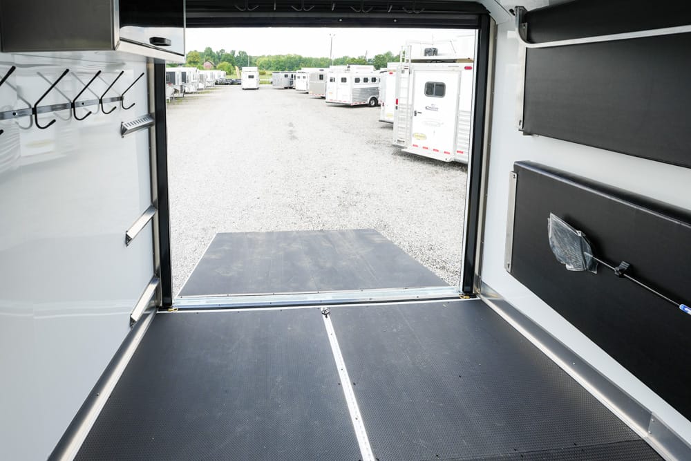 Interior of an empty trailer looking toward a gravel lot with parked trailers; ramp lowered to the ground.