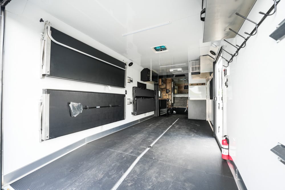 Interior of an empty ambulance with wall-mounted stretchers, cabinets, and a fire extinguisher at the doorway