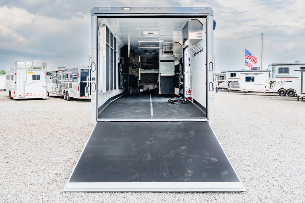 Open cargo trailer with a wide ramp leading into a mobile workshop, containing cabinets and equipment inside the trailer.