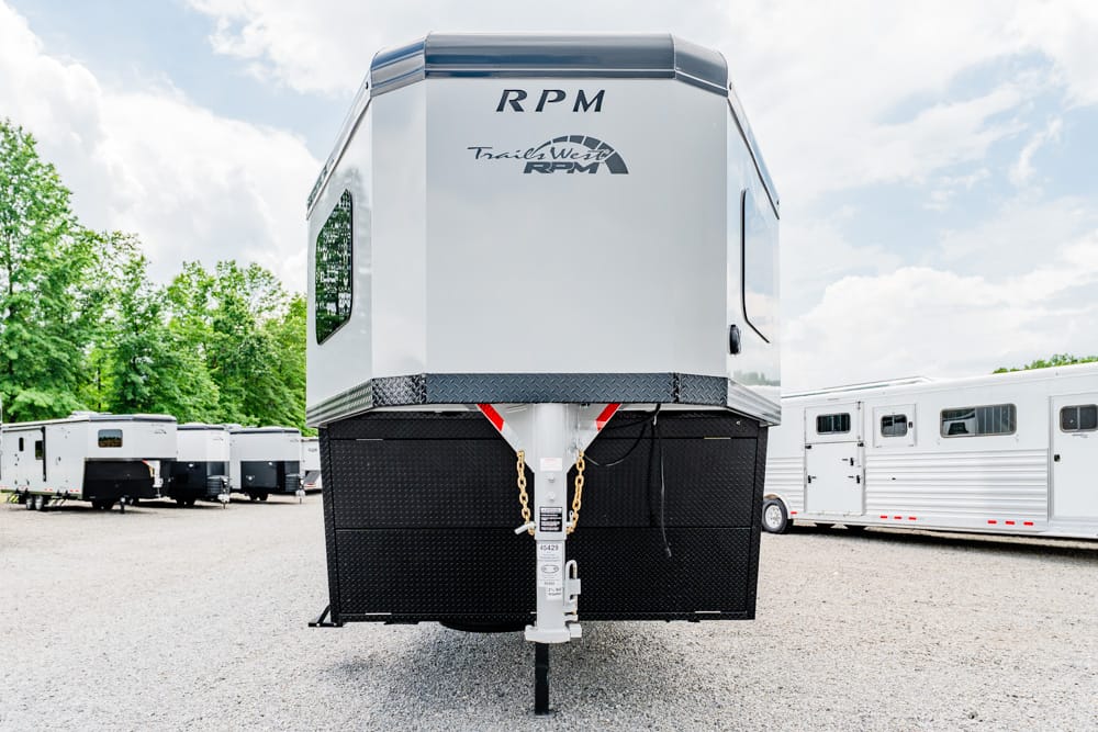 Front view of a silver RPM trailer on a gravel lot, with safety chains and hitch visible, others trailers in the background