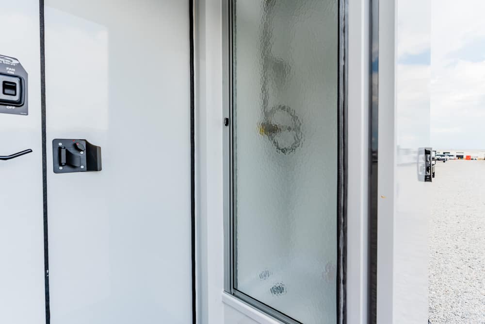 Exterior trailer/utility door with a frosted glass panel and black latch on a gravel lot outside.