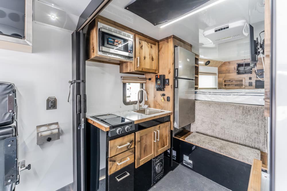 Compact RV kitchen with wooden cabinets, microwave above, sink, and two-burner stove.