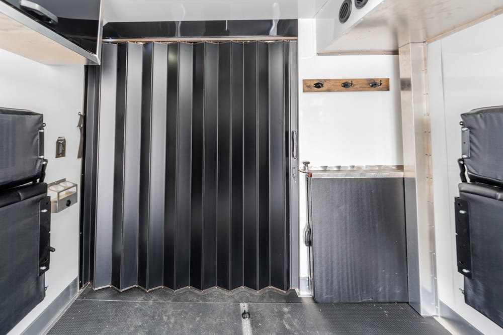 Interior of a vehicle with a black accordion partition, metal cabinet, and padded seats on both sides in white walls