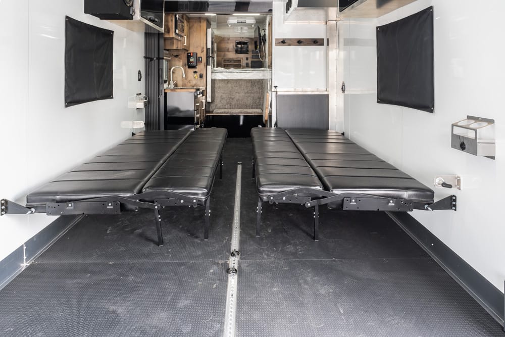 Interior of a medical transport vehicle with two black-folding stretchers extended side by side, ready for patient care