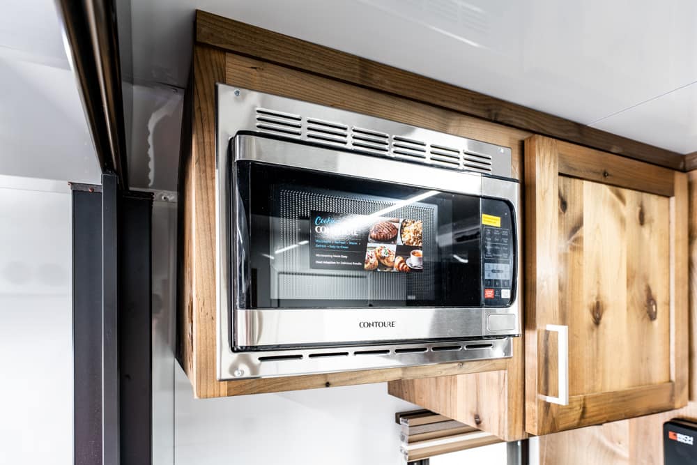 Stainless steel microwave oven mounted in a wooden cabinet with a control panel and display visible on the right.