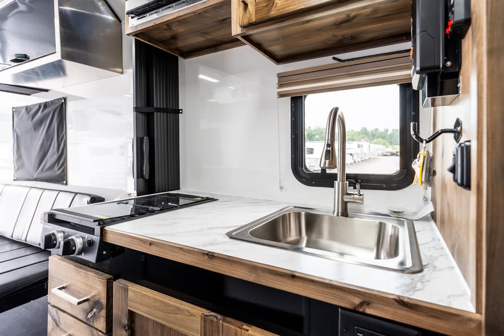 Camper van kitchenette with marble countertop, stainless steel sink, and compact stove.