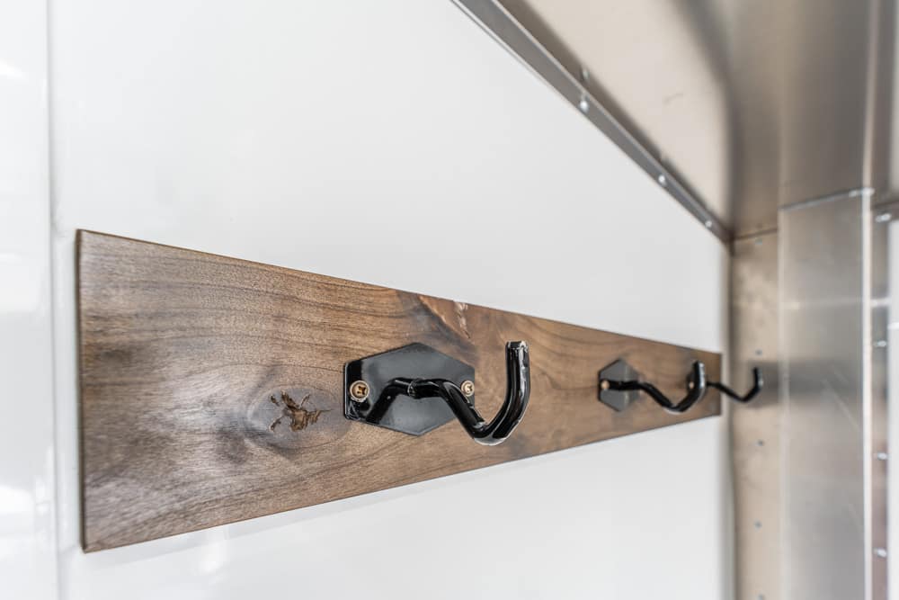 Wooden wall-mounted peg rail with three black metal hooks on a white wall