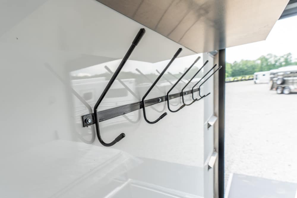 Row of black metal hooks mounted on a rail inside a white trailer wall, for hanging coats or gear.
