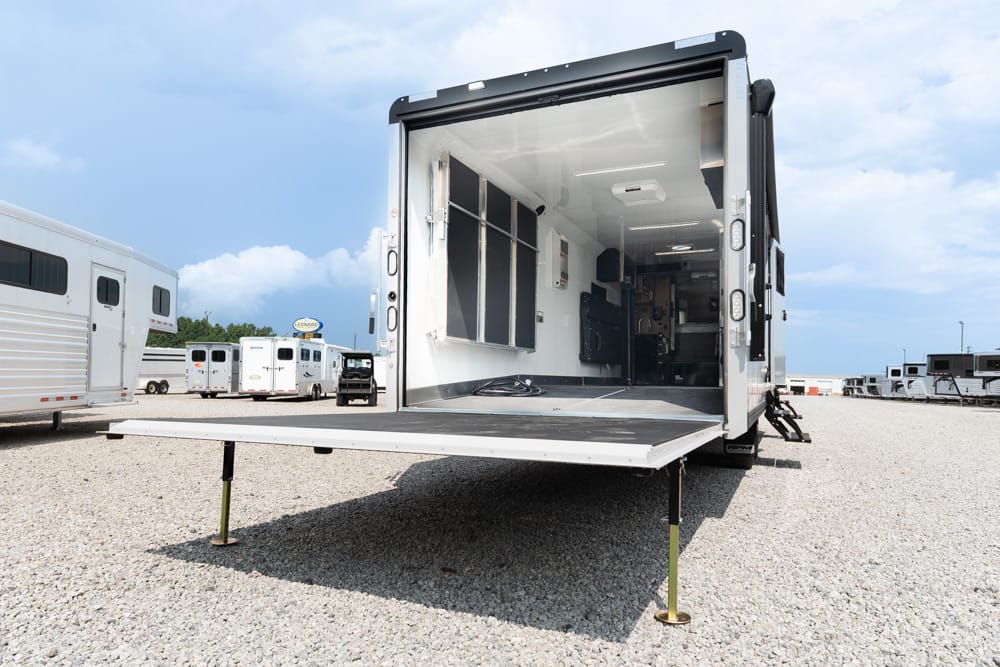 Open mobile workshop trailer with ramp lowered onto a gravel lot, interior cabinets and equipment visible