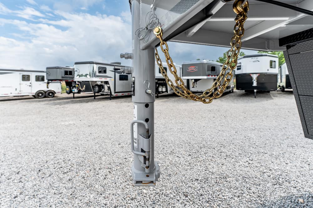RV trailer hitch with safety chains and jack in foreground; multiple travel trailers in a gravel lot behind. (informative)