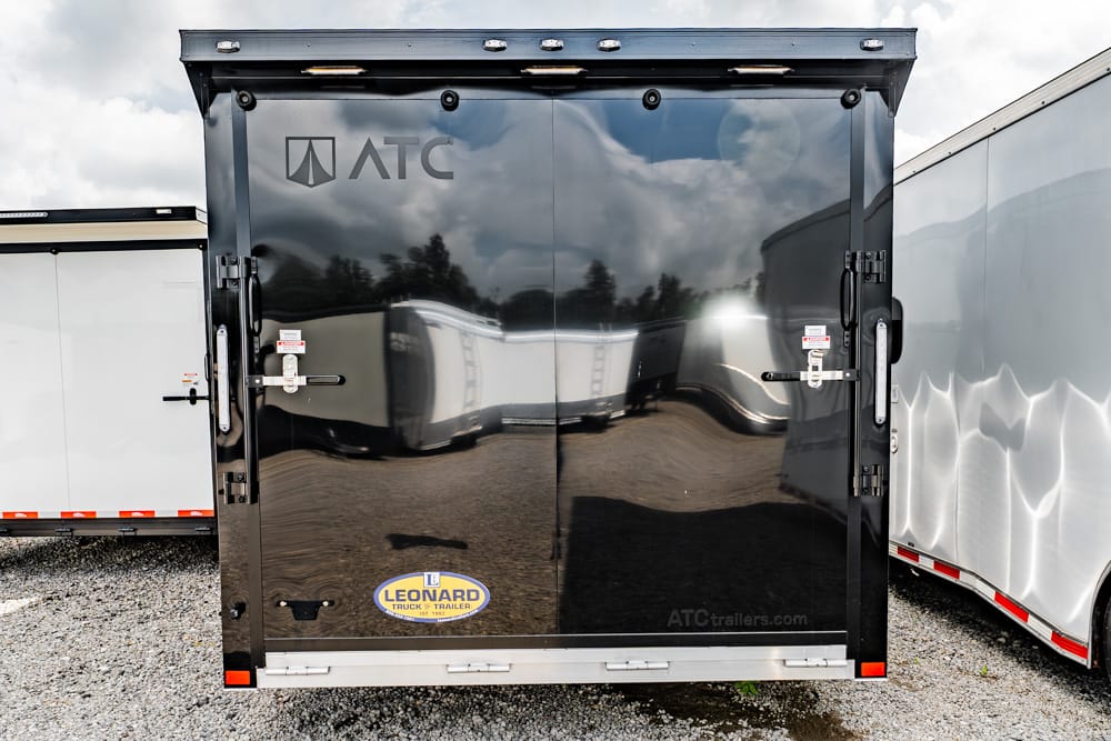 Rear of a glossy black ATC trailer with double doors, Leonard sticker, and reflections of nearby trailers.