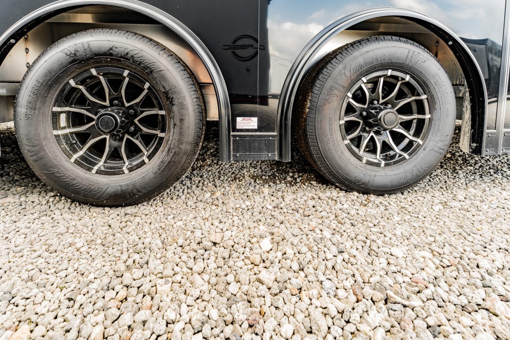 Dual rear wheels of a black trailer parked on a gravel surface