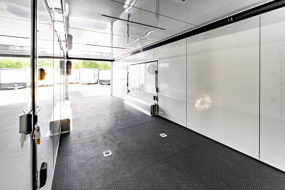 Interior of a clean white cargo trailer with glossy panels, black non-slip floor, and a rear doorway visible in the distance.