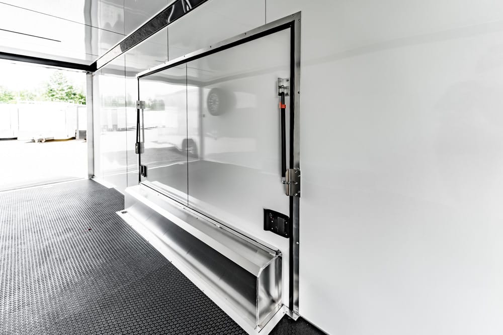 Interior of a white cargo trailer with a large flush metal door, metal trim, and a black textured non-slip floor.