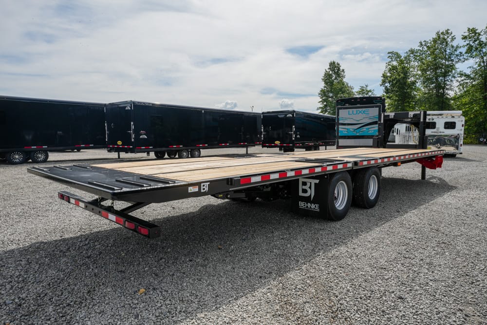Long flatbed trailer with a wooden deck and dual rear axles, parked in a gravel lot among other trailers; Behnke/BT branding visible on the side.