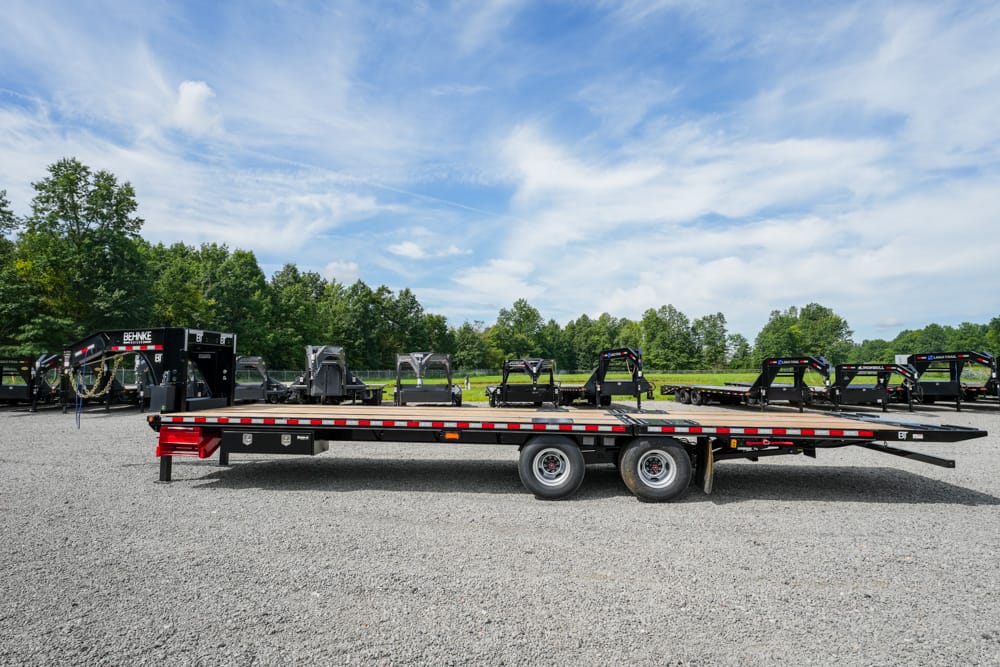 Long flatbed trailer on a gravel lot, with other trailers lined up in the background under a blue sky.