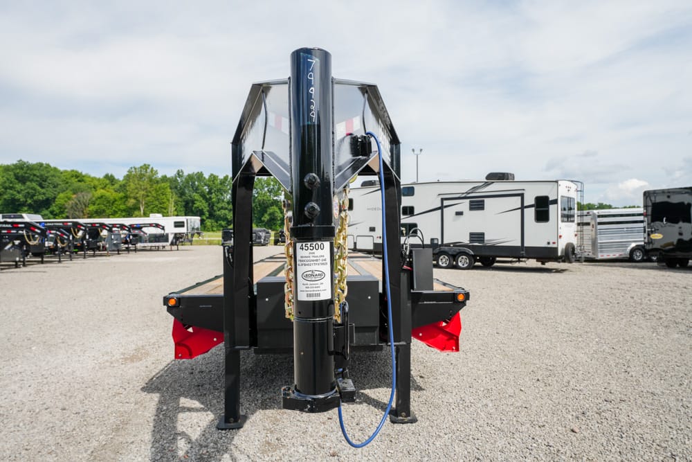 Gooseneck trailer hitch post with chains on a black flatbed trailer in an RV lot.