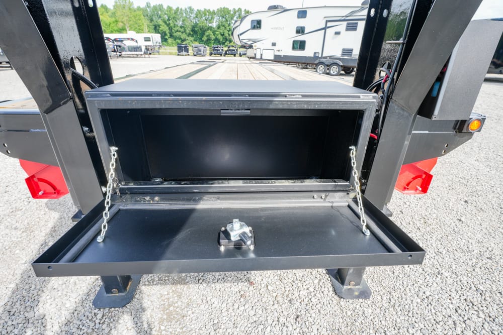 Open black metal storage compartment on a trailer, with chain supports and a hitch in the foreground.
