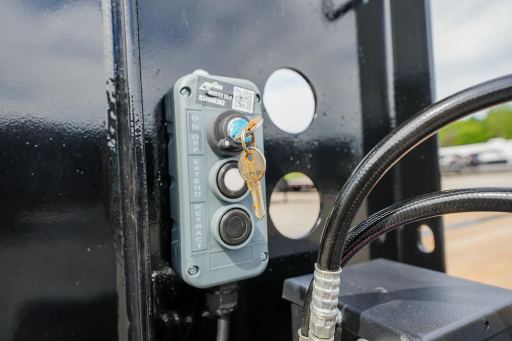 Blue-gray control panel with three buttons and a key hanging from a lock, mounted on a black metal frame near a hose or cable.