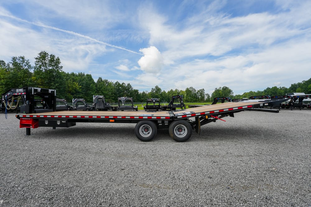 Flatbed trailer on a gravel lot with other trailers in the background and a blue sky above.