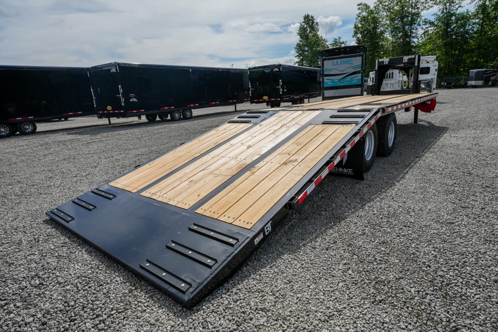 Flatbed trailer with a wooden deck parked on a gravel lot, with other trailers in the background.