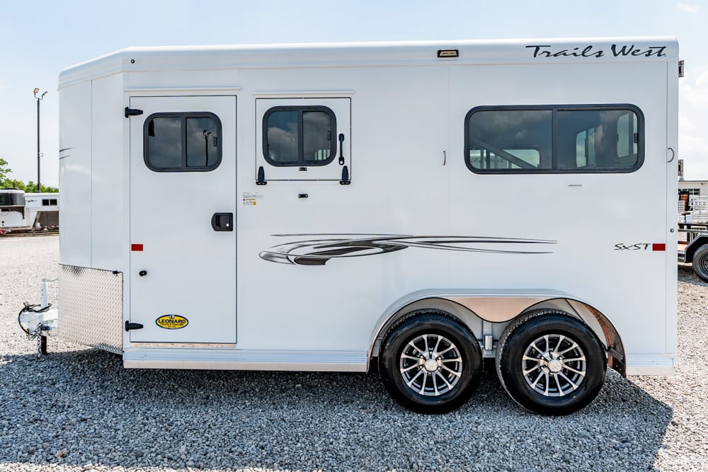 White Trails West travel trailer with dual axles and decorative graphics on a gravel lot, side view.