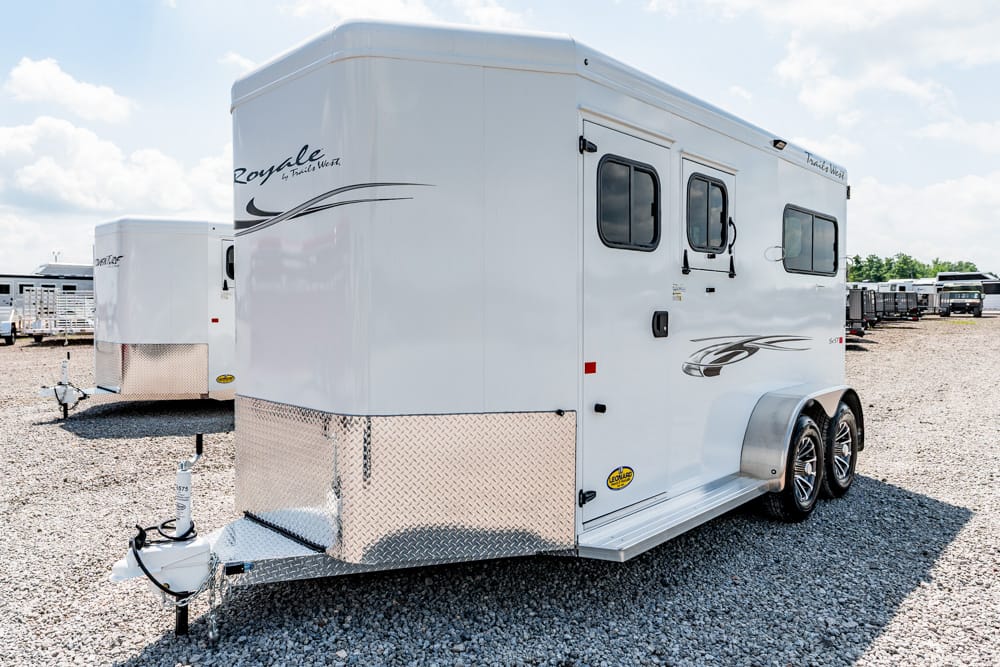 White dual-axle horse trailer with diamond-plate front parked on a gravel lot, with other trailers in the background and clear sky above.