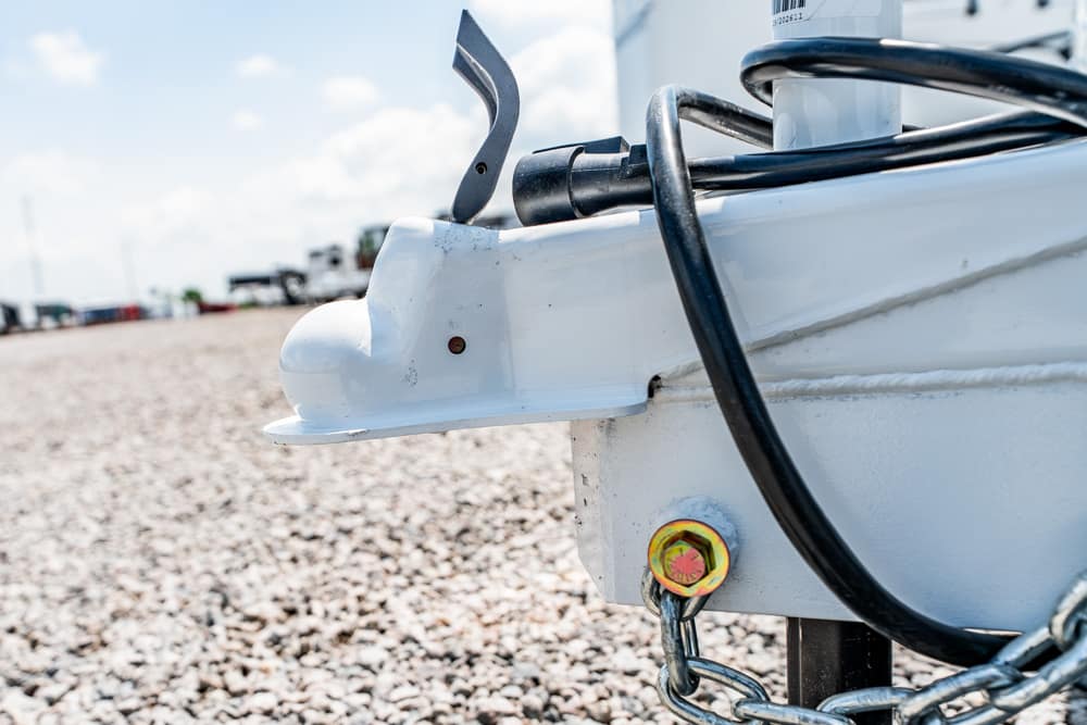 Close-up of a boat trailer hitch on a gravel surface with a yellow bolt and attached cables nearby.