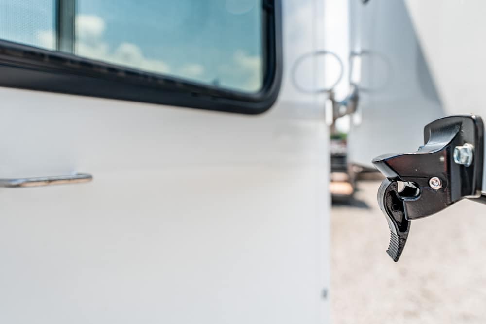 Close-up of a black door latch on a white trailer door, ready to be opened outside.