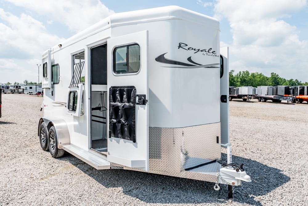 White Royale horse trailer with dual axles, open side door, and diamond-plate nose parked on a gravel lot.