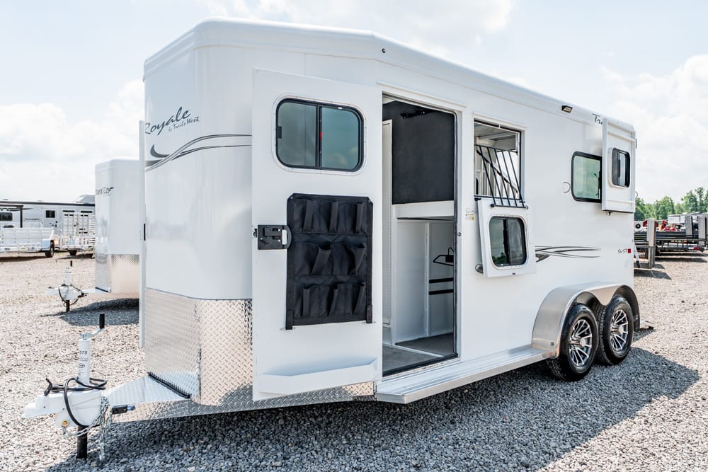 White travel trailer with an open side door and storage pockets, parked on a gravel lot.