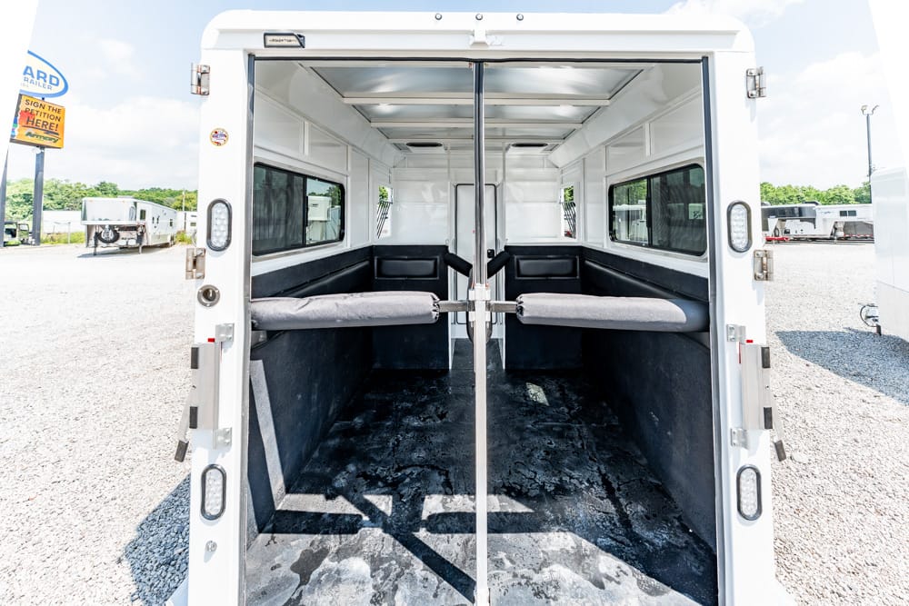 Open inside of a white trailer with gray cushioned benches along the sides and a central divider, doors wide open.