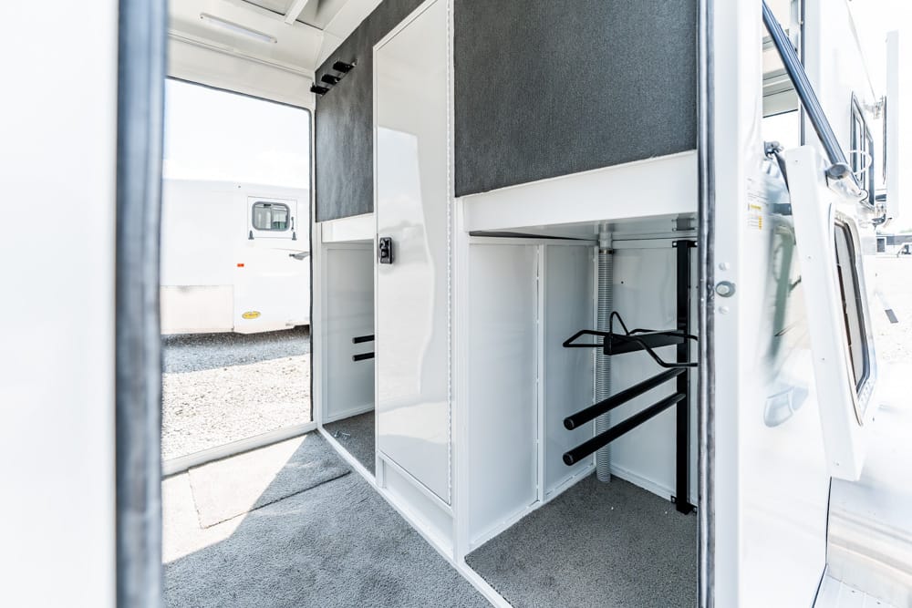 Interior of a white utility vehicle showing built-in storage cabinets, hanging bars, and a carpeted floor for organized gear transport