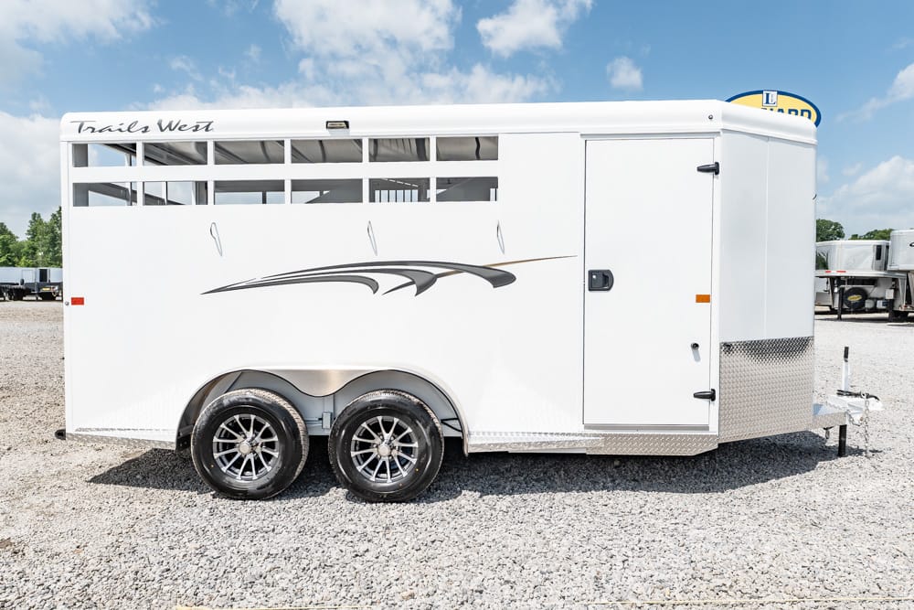 White horse trailer with decorative gray graphics parked on a gravel lot; dual axles and a side access door visible.