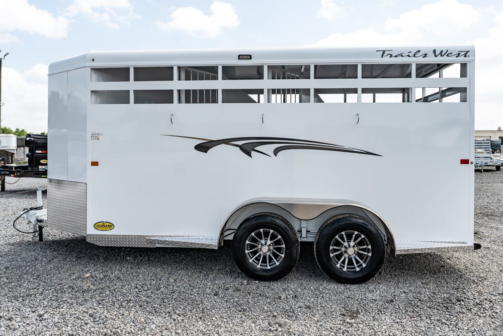 White Trails West horse trailer with a two-axle design and decorative swoosh, parked on a gravel lot.