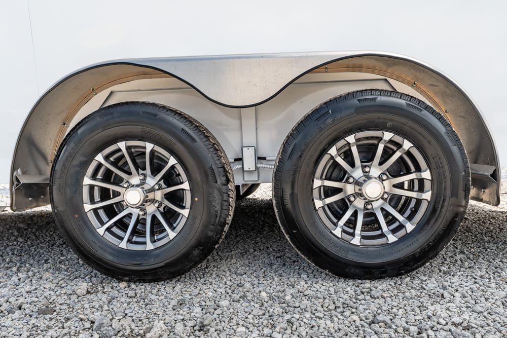 Dual-axle trailer wheels with metal fenders on a gravel surface, showing two alloy rims and tires side by side.”,”Close-up of twin wheels on a utility trailer under a curved fender, parked on gravel.”,”Two alloy wheels on a trailer’s axle, with protective fenders and a gravel ground.”,”Pair of trailer wheels with matching rims, under a silver wheel well, on small rocks.”,”Wheels and fenders of a dual-axle trailer resting on a gravel surface.”]}```json to=final code```?``` hmm (This final should be proper JSON inside the required format)``` The assistant should output: {