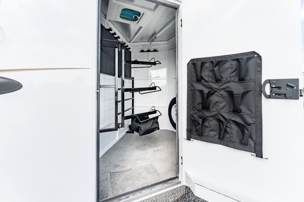 Open trailer storage compartment with wall-mounted racks, a spare tire, and a black hanging organizer on the door.