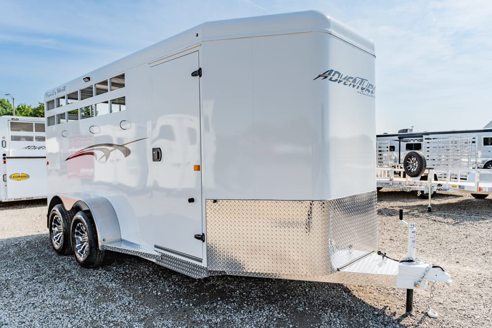 White Adventure horse trailer with diamond-plate front, dual axles, and a front hitch in a gravel lot.