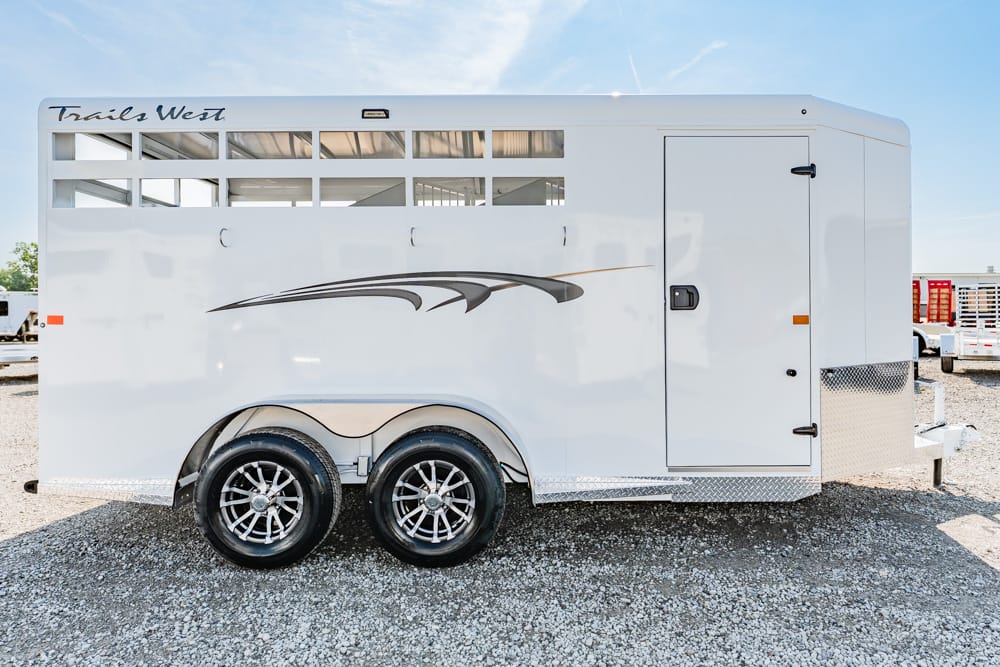 White Trails West horse trailer with decorative graphics, two axles, and a side entry door on a gravel lot.
