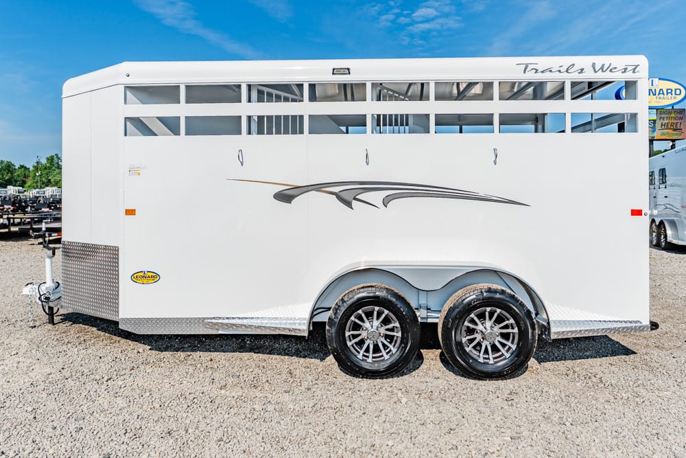White Trails West horse trailer with two axles and decorative swoosh graphic, parked on gravel.