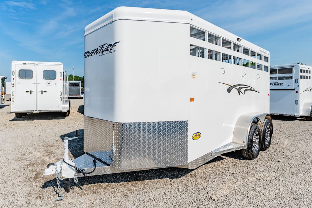 White horse trailer with diamond-plate front and dual wheels parked on a gravel lot, hitch and safety chains visible in the foreground.