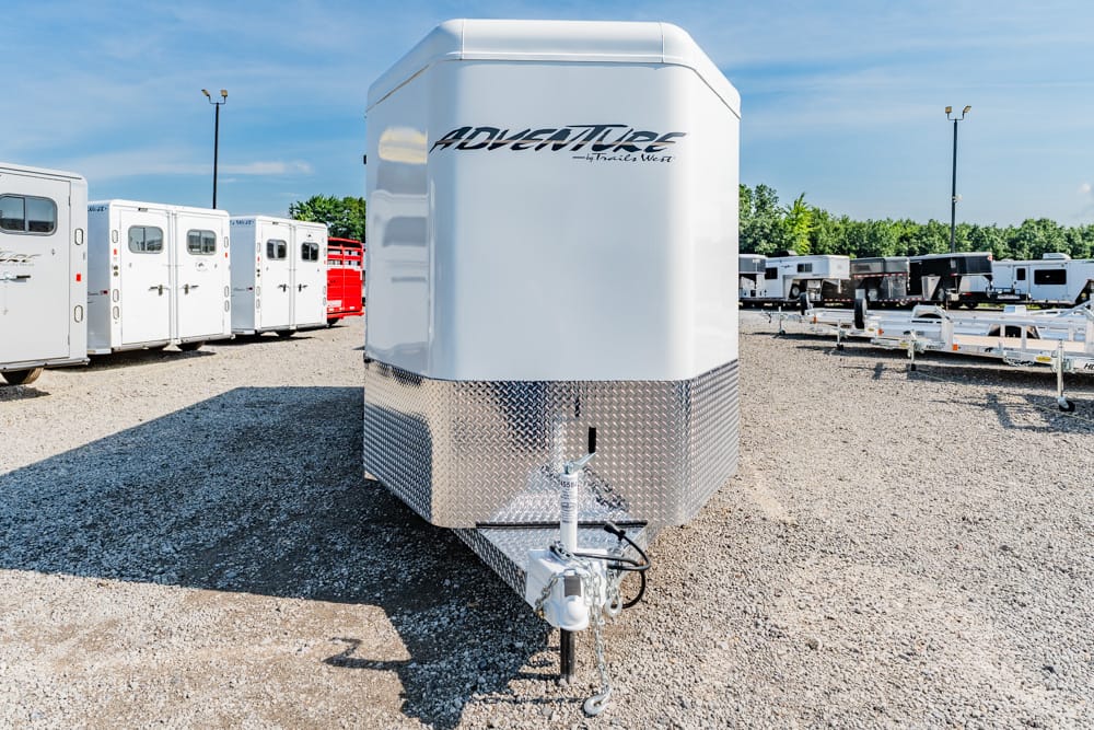 White Adventure by Trails West horse trailer with diamond-plate front, parked among other trailers in a gravel lot.