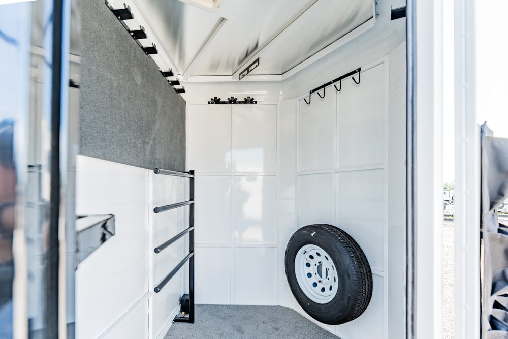 Interior of a white utility trailer with peg hooks, cabinet drawers, a mounted spare tire, and a gray carpeted floor