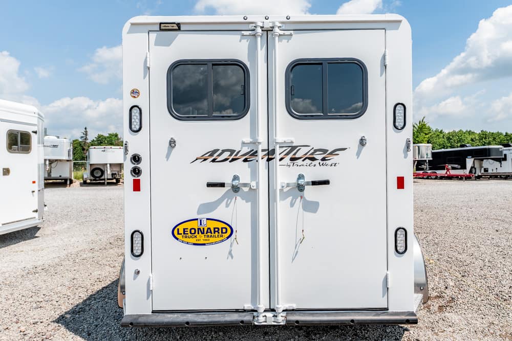 Back of a white travel trailer with double doors, two small windows, and an 'Adventure by Trails West' decal; Leonard Trailer sticker on lower left door.