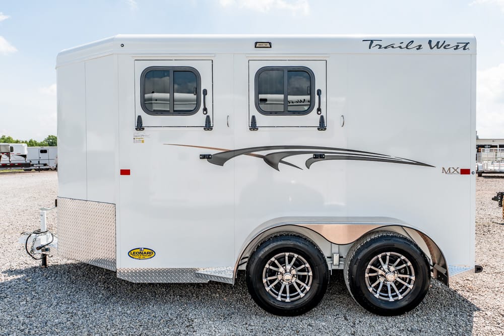 White Trails West horse trailer with two small windows, dual axles, and decorative graphics on a gravel lot.
