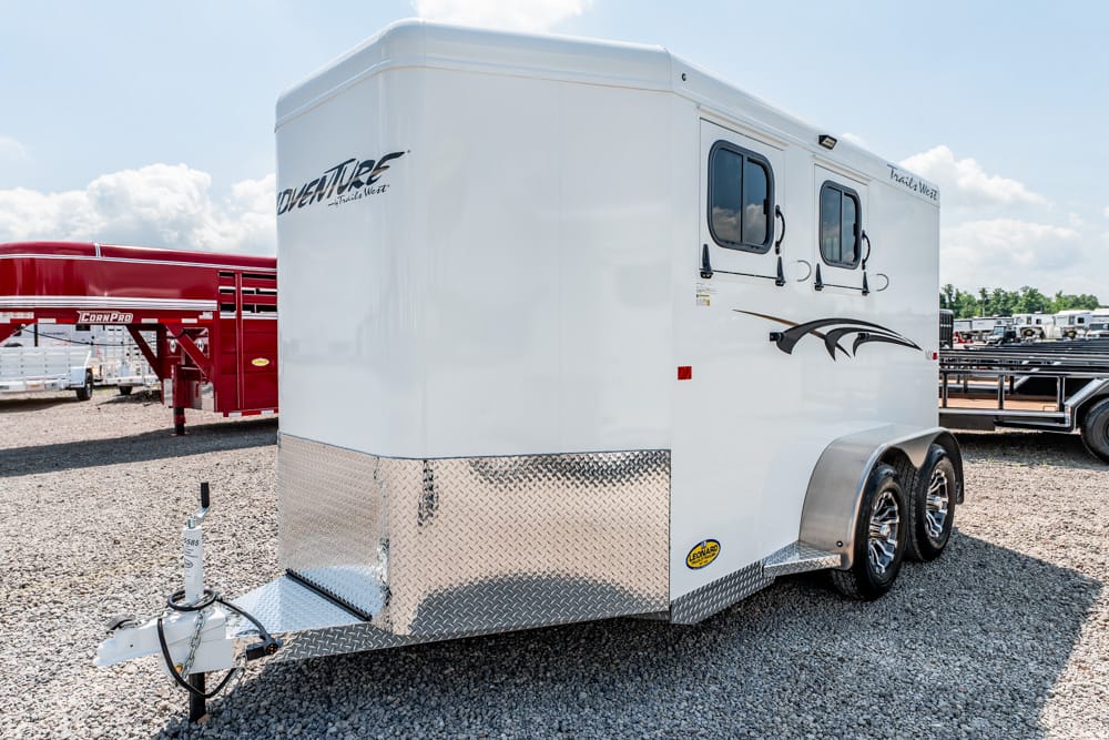 White twin‑axle horse trailer with diamond‑plate front, parked on a gravel lot.